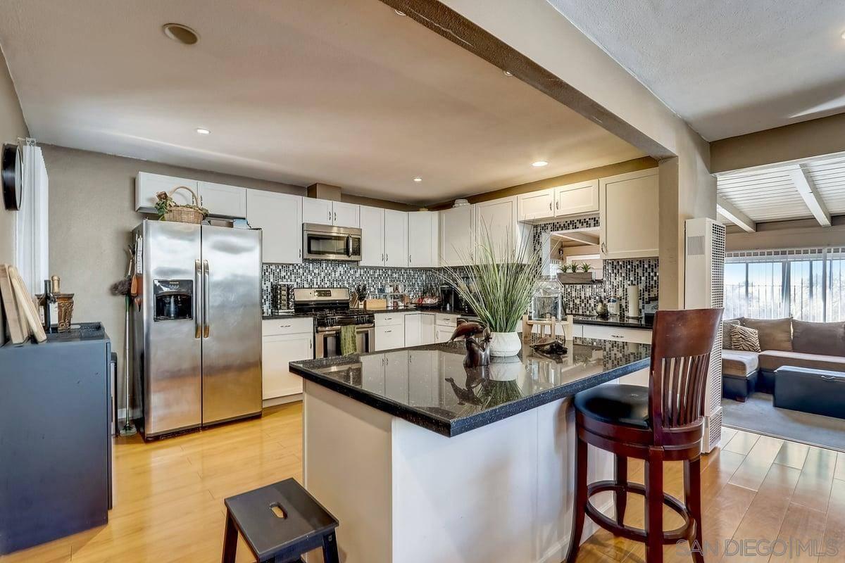 A kitchen with  dark countertops, tile backsplash, stainless appliances, light wood floor